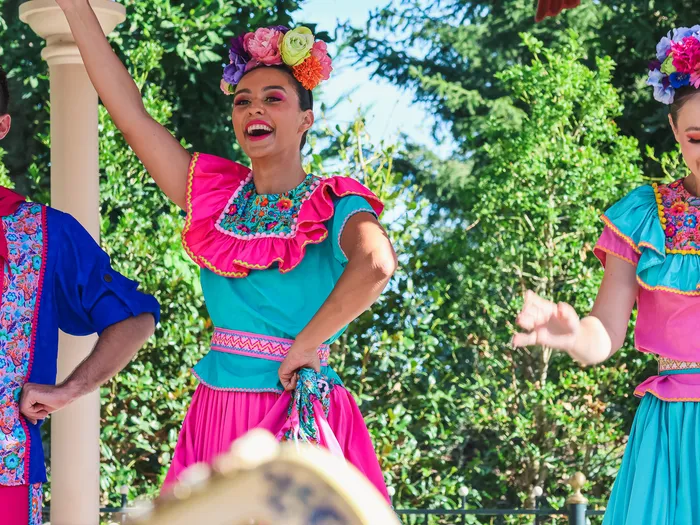 Dancers in pink and turquoise floral outfits, all smiles, during Miguel’s Fiesta Latina at Disneyland Paris