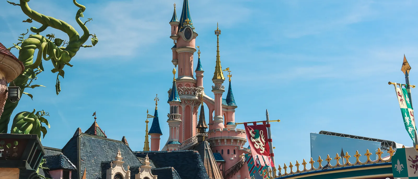 Sleeping Beauty Castle at Disneyland Paris, with its pink towers and blue roofs, seen from Fantasyland under a clear sky.