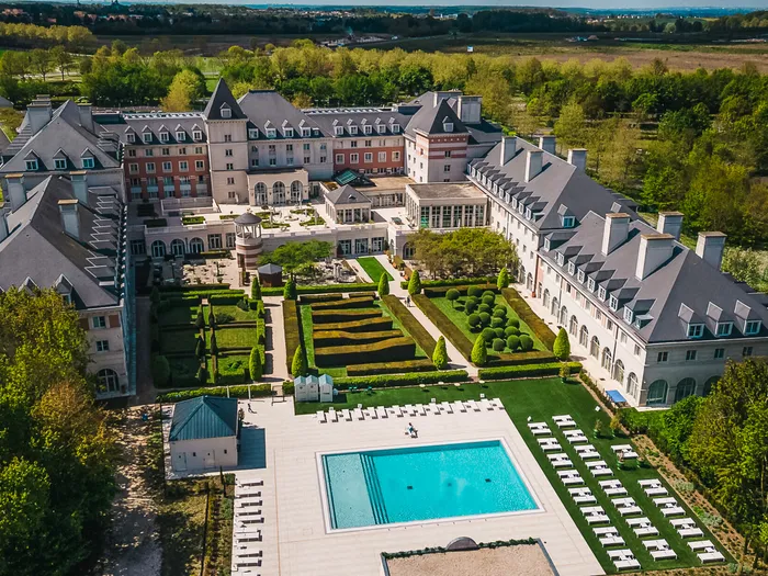 Façade château du Dream Castle Hotel avec jardins à la française et piscine, vue du ciel