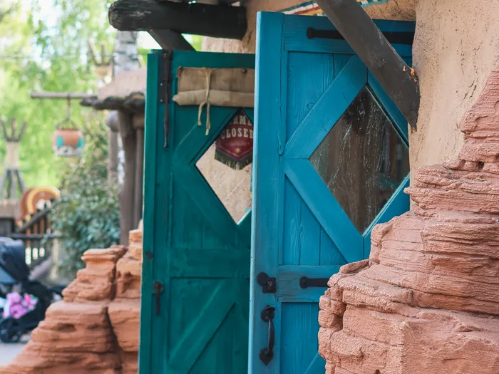 Turquoise wooden doors with diamond windows at Pueblo Trading Post, under a log awning among the red rocks of Frontierland, Disneyland Paris