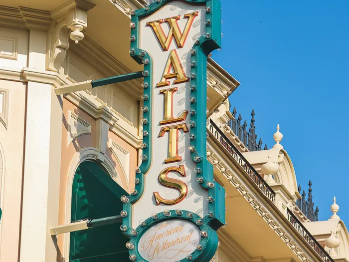 Enseigne verticale lumineuse « Walt’s an American Restaurant » sur une façade de Main Street U.S.A. sous ciel bleu