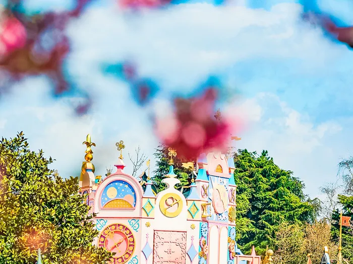Façade pastel rose et bleue d’it’s a small world encadrée de fleurs de cerisier roses à Fantasyland