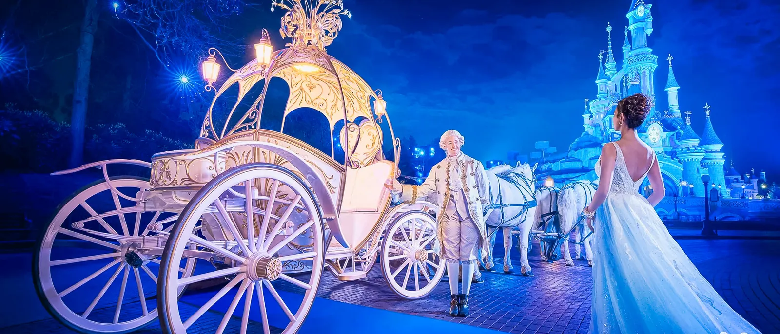 Mariée en robe blanche marchant vers un carrosse illuminé de Cendrillon, château bleuté en arrière-plan la nuit à Disneyland Paris.