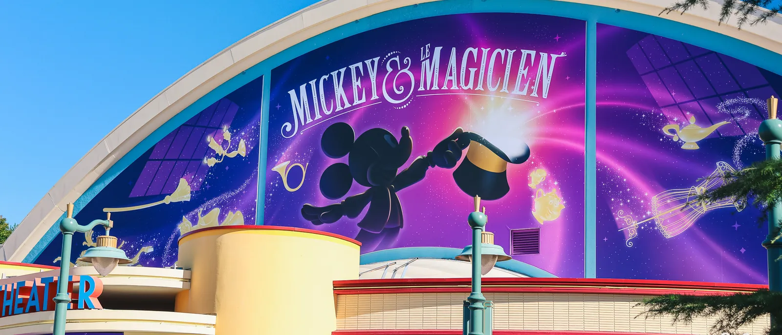 Façade violette du théâtre annonçant le spectacle Mickey et le Magicien, avec la silhouette de Mickey et un chapeau doré.