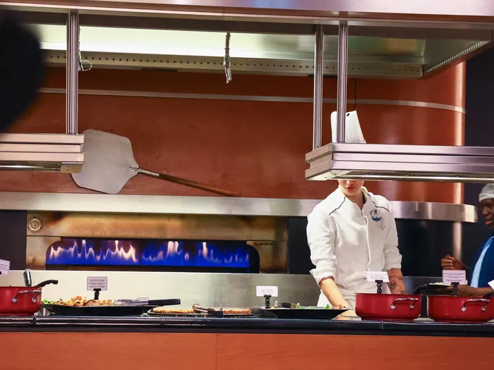 Cuisiniers au comptoir ouvert du Downtown Restaurant, devant le four à flamme bleue et des casseroles rouges
