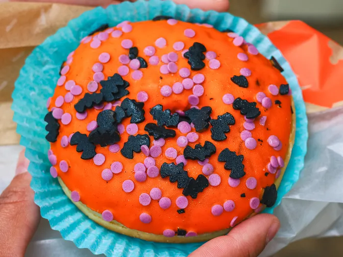 Donut au glaçage orange, vermicelles violets et chauves-souris noires tenu en main à la Cookie Kitchen