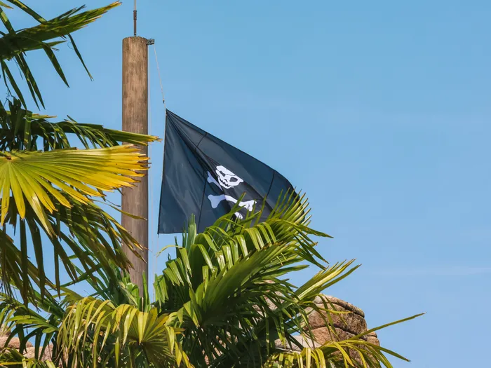 Drapeau noir à tête de mort flottant en haut d'un mât au-dessus des palmiers de Pirates of the Caribbean, ciel bleu