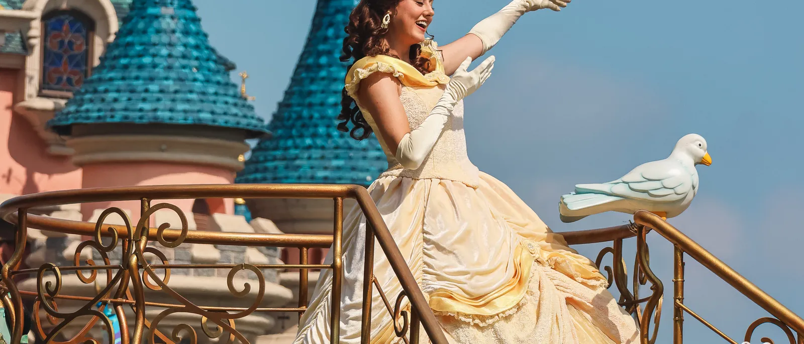 La princesse Belle en robe jaune salue la foule depuis un char de parade, devant les tours bleues du château.