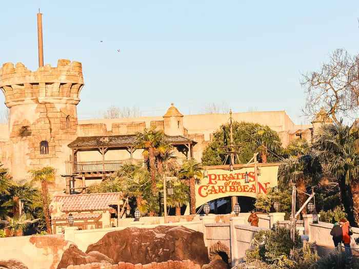 Fort en pierre, palmiers et enseigne rouge de l’attraction Pirates of the Caribbean à Adventureland