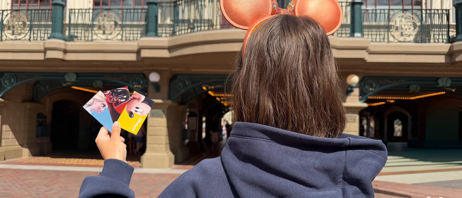 De dos, une visiteuse à oreilles de Minnie orange tient trois billets d’entrée devant la gare de Main Street à Disneyland Paris.
