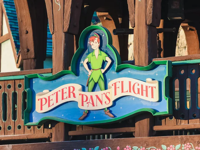 Enseigne sculptée de Peter Pan’s Flight avec le personnage, fixée sur la façade en bois de l’attraction à Fantasyland.