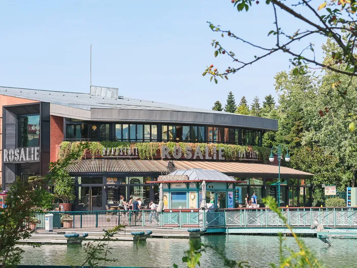 Façade de la Brasserie Rosalie et sa terrasse au bord du lac du Disney Village sous un ciel bleu.