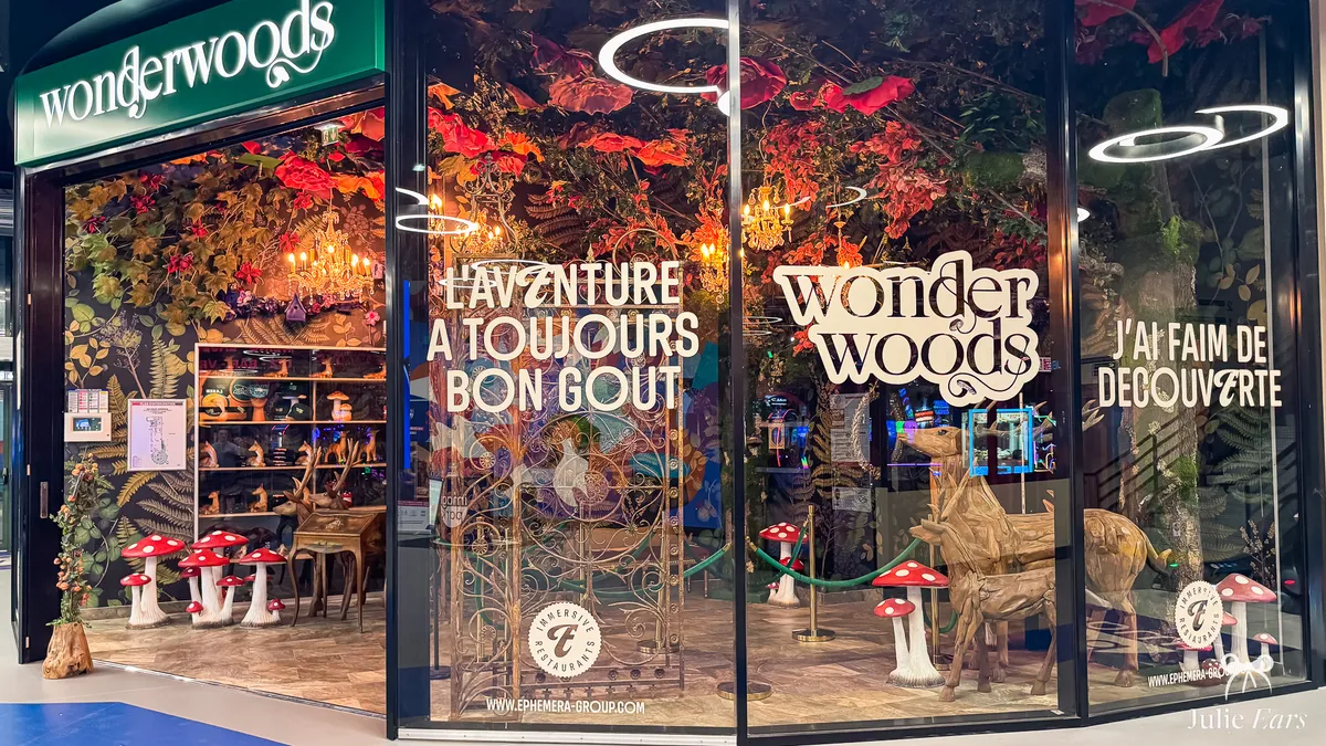 Wonderwoods restaurant shopfront at Imagi Park, its window decorated with foliage, red flowers, chandeliers, spotted red toadstools and wooden deer