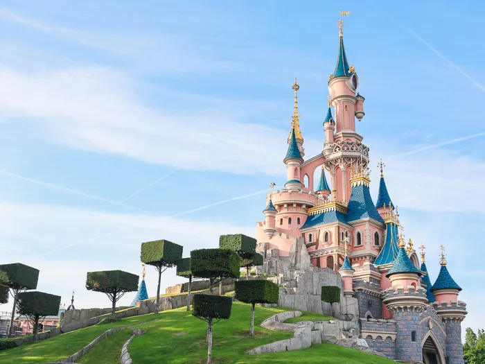 Le Château de la Belle au Bois Dormant rose et bleu sur sa colline arborée, sous un ciel bleu à Disneyland Paris.