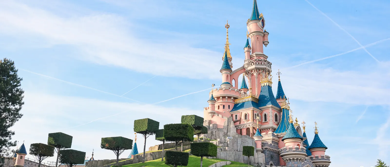 Le Château de la Belle au Bois Dormant rose et bleu sur sa colline arborée, sous un ciel bleu à Disneyland Paris.