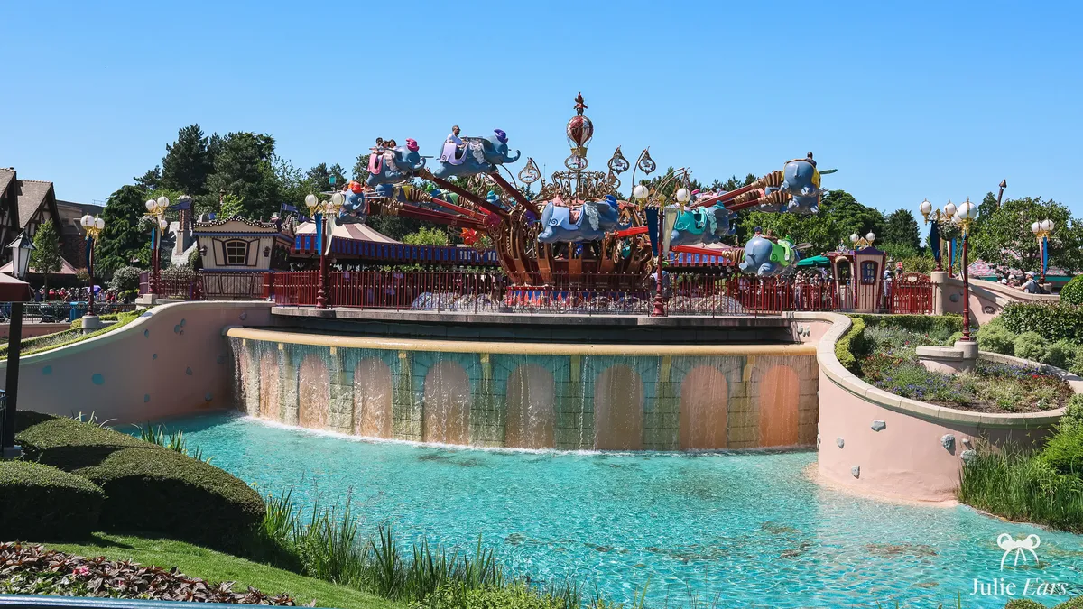 Dumbo the Flying Elephant in Fantasyland at Disneyland Paris, its flying elephants full of visitors above a waterfall and a turquoise pool