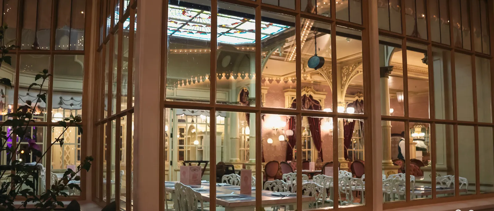 Salle du Plaza Gardens vue de nuit à travers les grandes vitres, tables dressées et lumières chaudes.