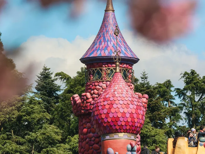 Tour rose et violette du Labyrinthe d’Alice dépassant des arbres, à Fantasyland.