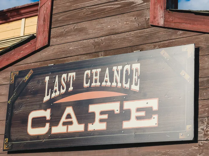 Enseigne peinte Last Chance Cafe fixée sur le mur en planches de bois d’un bâtiment western, à Frontierland.