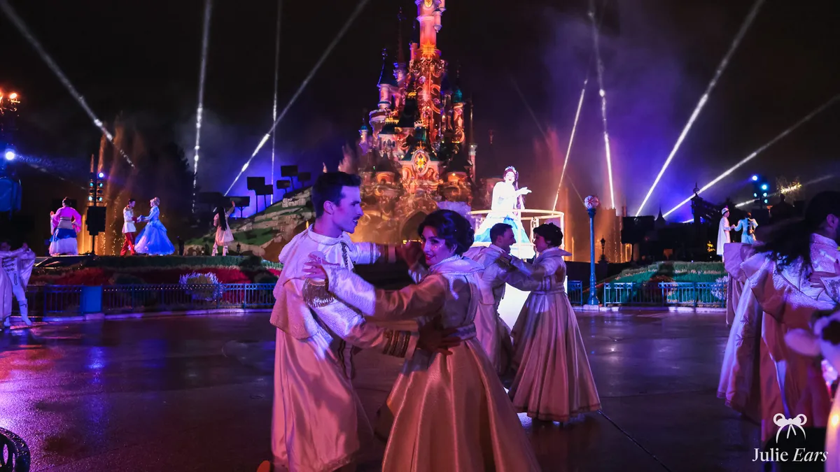 Dancers in cream and gold ballroom outfits waltzing on the wet ground of Central Plaza before the illuminated castle, at Christmas Ball Night 2025