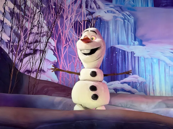 Le bonhomme de neige Olaf souriant devant une cascade gelée, scène animée de l'attraction Frozen Ever After.