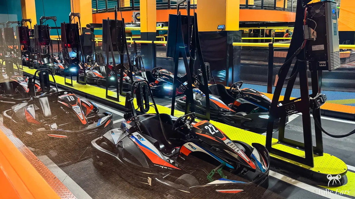 Numbered electric karts plugged in on the two-level indoor SpeedPark track at Imagi Park, Val d’Europe, with orange pillars