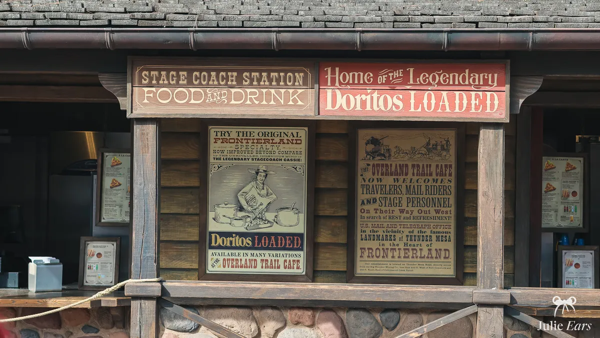 Overland Trail Café counter in Frontierland, Disneyland Park, with wooden Stage Coach Station and Doritos Loaded signs and Western posters