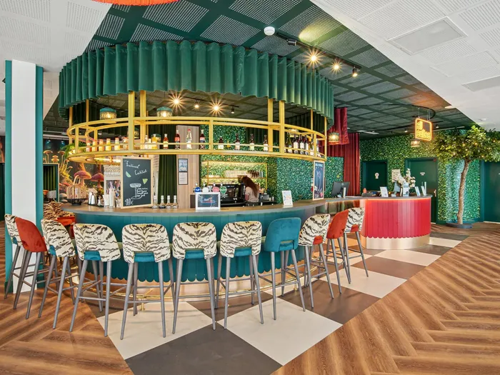 Bar coloré de l’Appart Hôtel All Suites Val d’Europe, comptoir en velours, tabourets et mur végétal, sol en damier et parquet.