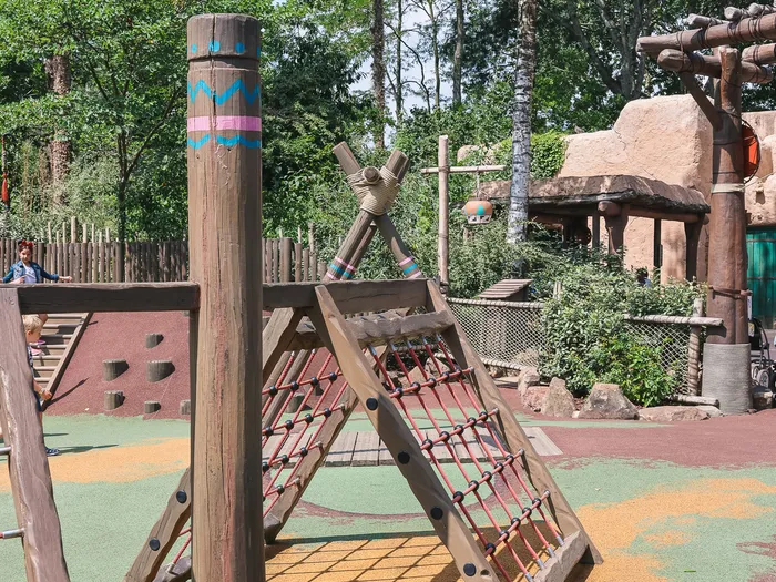 Structure d’escalade en bois avec totem peint et filet de corde sur le sol souple du Frontierland Playground