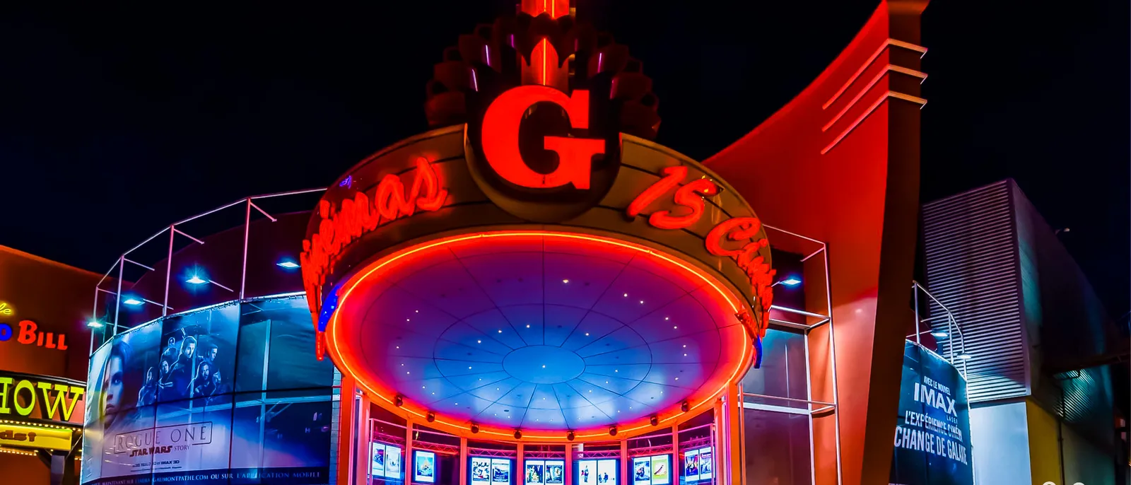 Façade rouge néon du cinéma Gaumont au Disney Village, éclairée de nuit avec ses affiches de films.