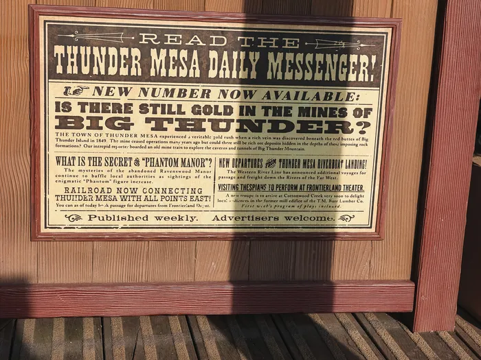Panneau encadré du journal Thunder Mesa Daily Messenger devant la terrasse en bois du Last Chance Cafe à Frontierland