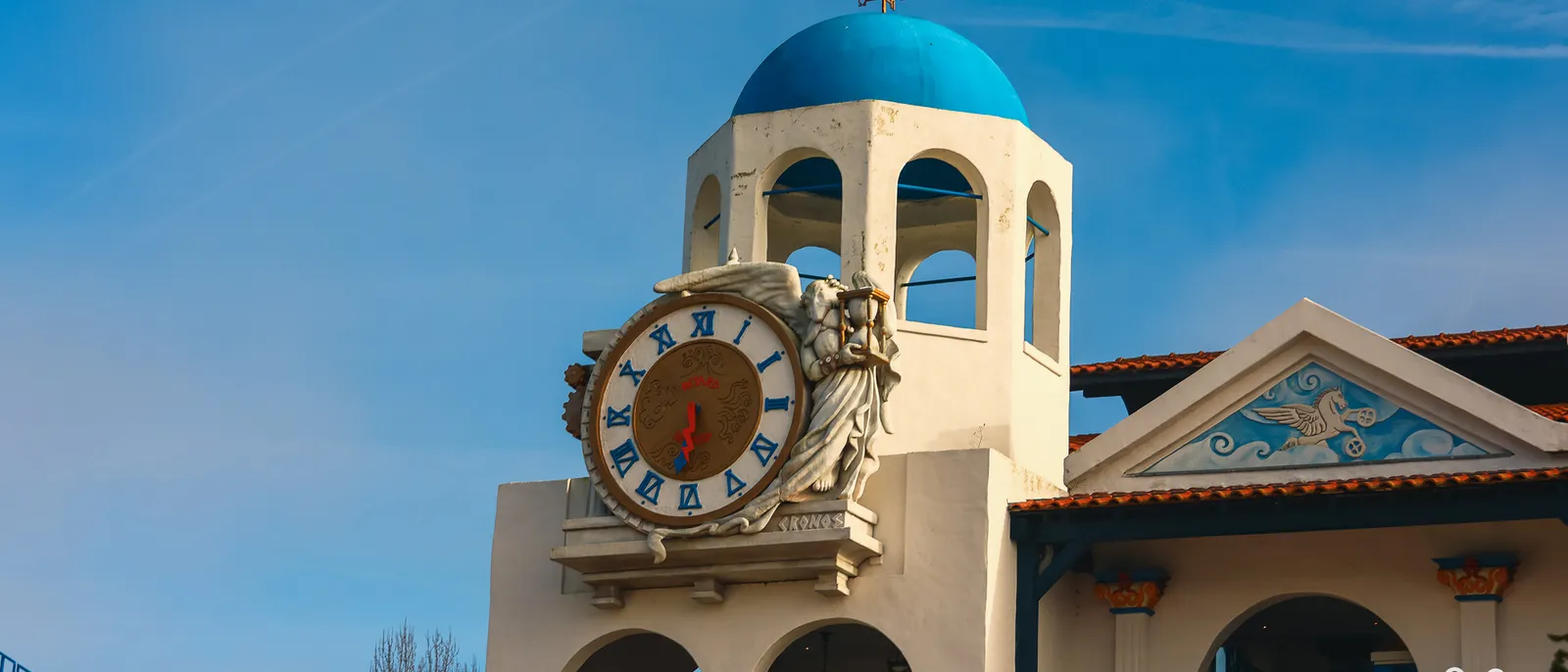 Tour blanche à coupole bleue de la gare de Pégase Express, horloge dorée à chiffres romains encadrée de chevaux ailés