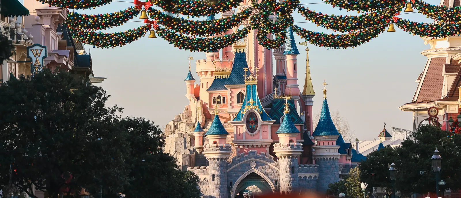 Guirlandes de Noël à boules et clochettes tendues au-dessus de Main Street, château de la Belle au Bois Dormant au loin.