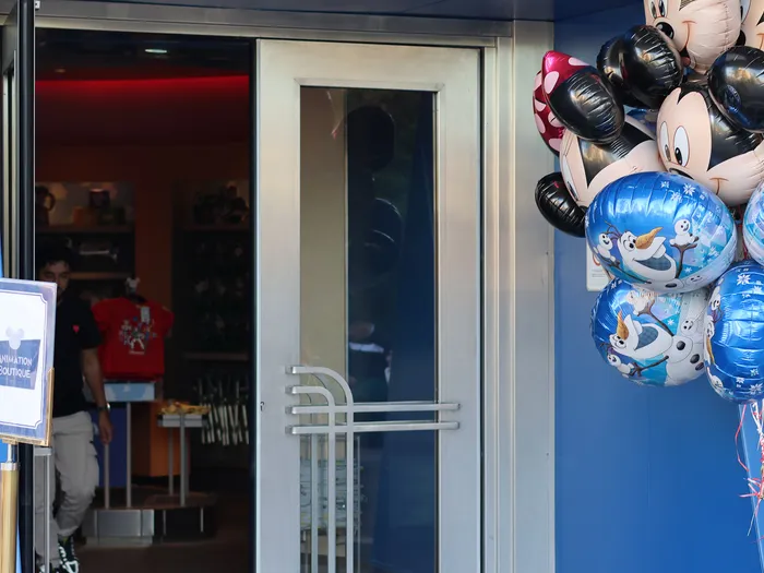 Entrance to the Animation Boutique at Disneyland Paris, blue frontage and open glass door, with a bunch of Mickey and Olaf balloons on the right.
