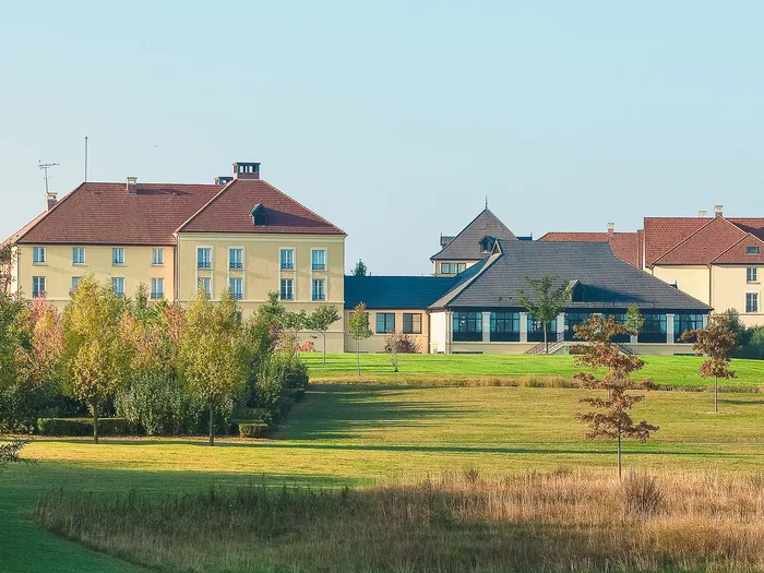 Bâtiments de l’hôtel Campanile Val de France derrière une prairie aux teintes d’automne.