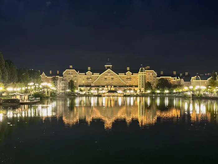 Façade du Newport Bay Club éclairée la nuit et reflétée dans le lac Disney.