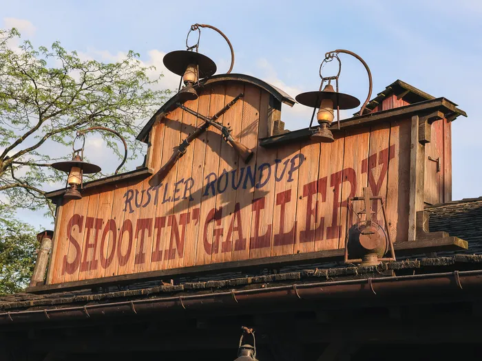 Enseigne en bois du Rustler Roundup Shootin’ Gallery, fusils croisés et lanternes, à Frontierland.