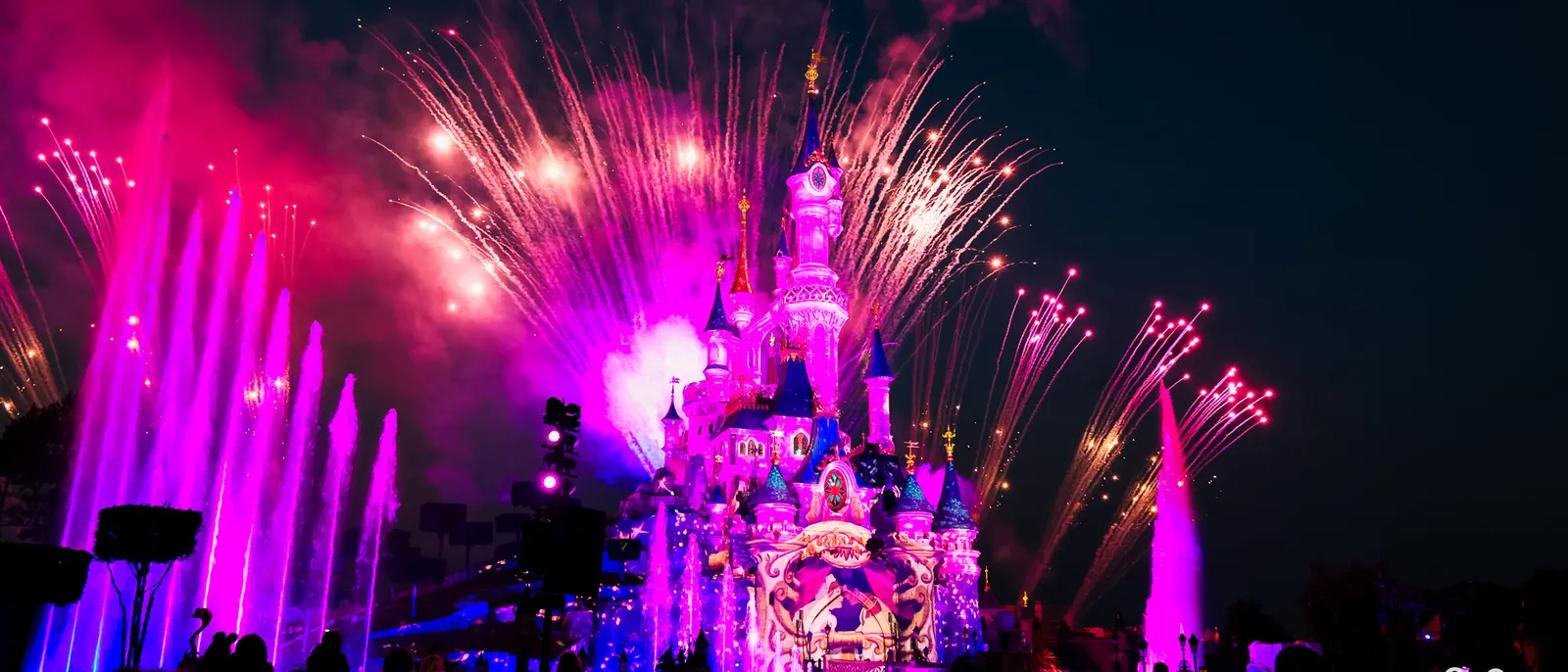 Feu d’artifice rose et jets d’eau illuminés devant le château de la Belle au Bois Dormant, la nuit à Disneyland Paris