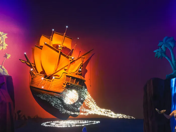 Galion volant illuminé laissant une traînée d’étincelles au-dessus de l’eau dans une scène du parcours de Peter Pan’s Flight.