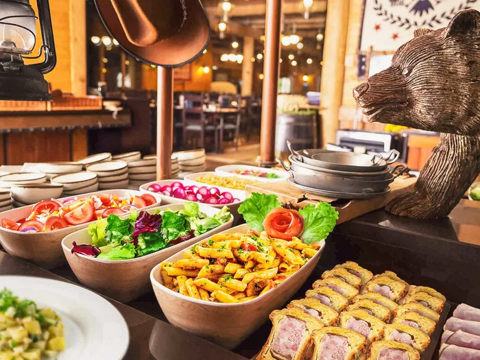 Buffet garni de salades, pâtes et tourtes au Crockett’s Tavern, avec statue d’ours et lanterne de trappeur