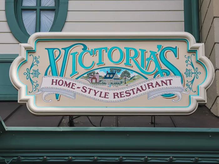 Enseigne turquoise Victoria’s Home-Style Restaurant ornée d’un paysage de campagne, sur Main Street USA.