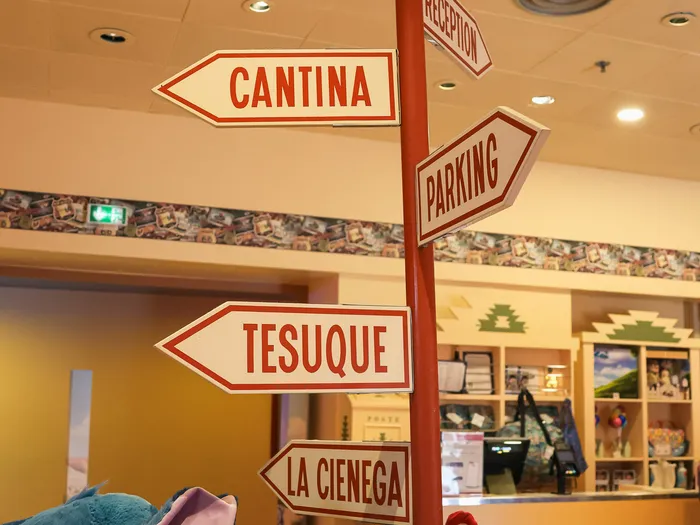 Post with red and white signposts (Cantina, Parking, Tesuque) above Stitch soft toys