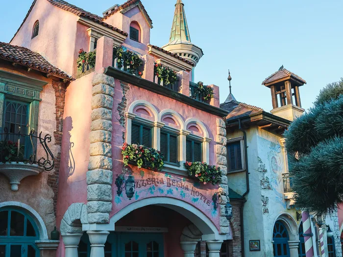 Façade rose italienne de la Pizzeria Bella Notte, clocheton et jardinières fleuries au-dessus de l’entrée voûtée à Fantasyland.