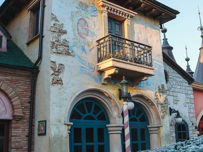 Tour ocre à campanile et balcon de la Pizzeria Bella Notte, fresque murale au-dessus des portes bleues cintrées à Fantasyland.