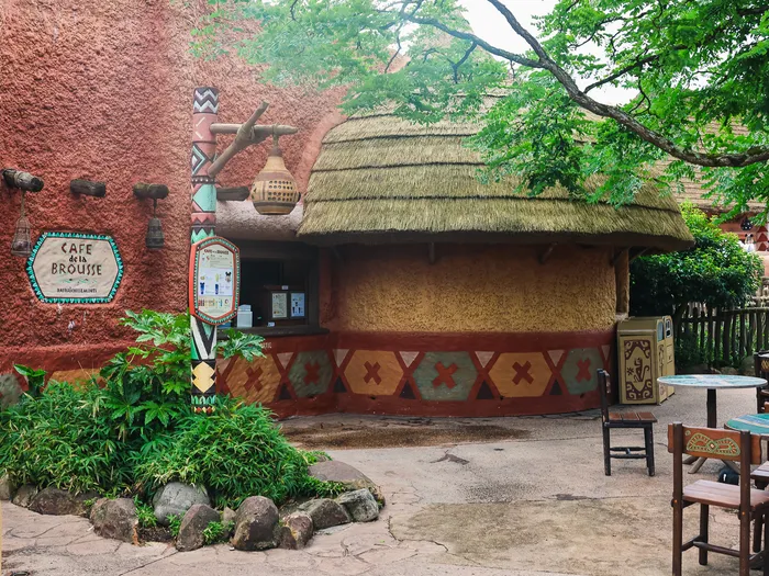 Façade au toit de chaume du Café de la Brousse à Adventureland, avec sa terrasse et ses tables en bois.