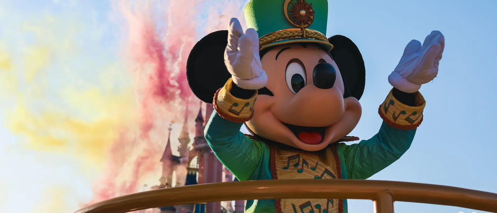 Mickey en costume vert à notes de musique salue devant le château, fumées colorées au Disney Music Festival à Disneyland Paris.