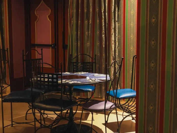Table ronde et chaises en fer forgé devant des tentures rayées dans la salle de l’Agrabah Café