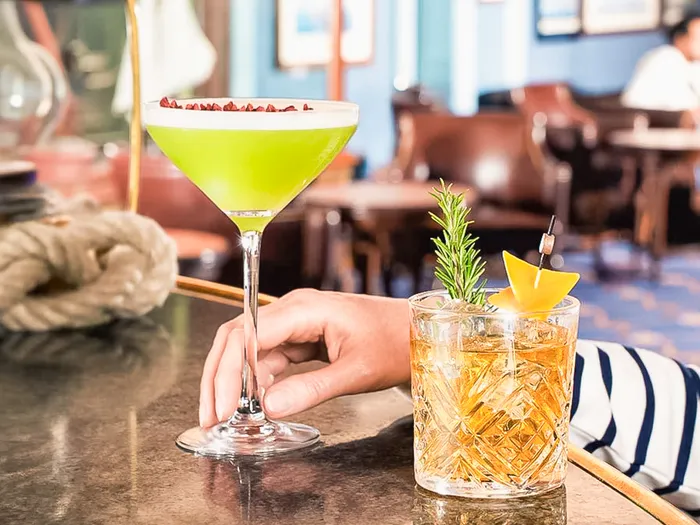 Deux cocktails, un vert en verre à martini et un ambré, sur le comptoir du bar Captain’s Quarters au Disney Newport Bay Club