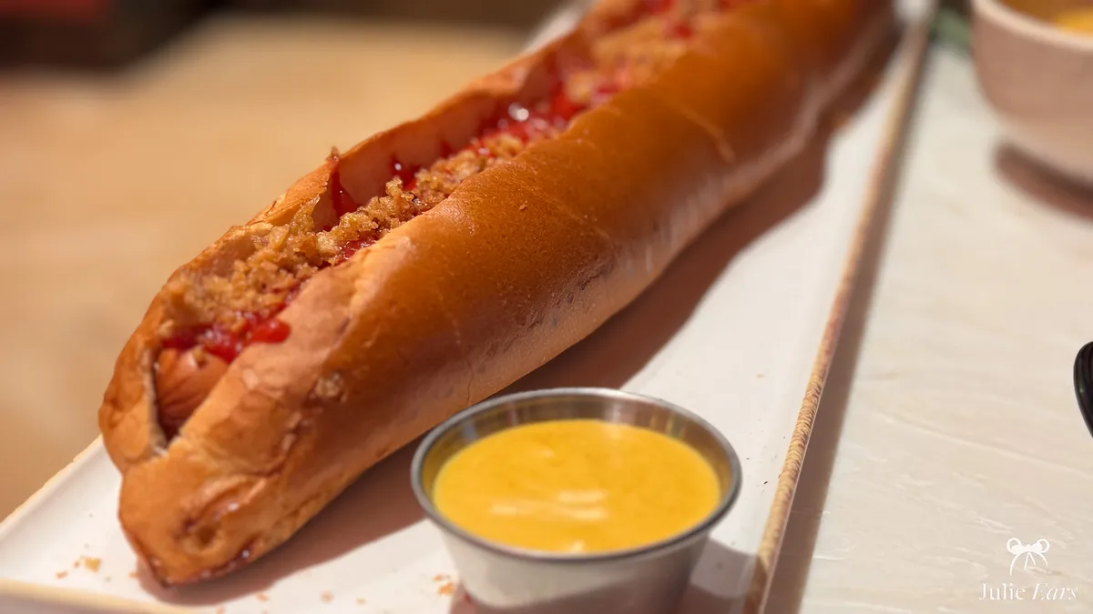 Giant hot dog topped with ketchup and crispy fried onions, with a cheese sauce on the side, at the Sports Bar in Disney Village.