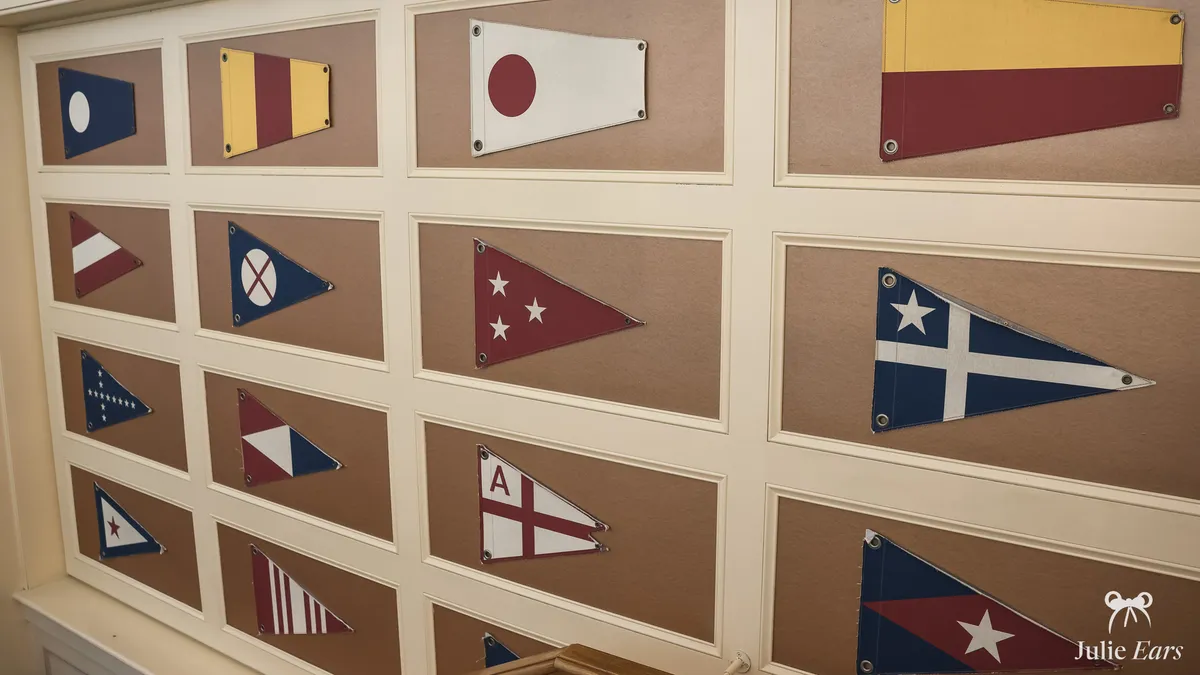 Navy, white, burgundy and yellow nautical pennants on cream moulded wall panels above a wooden handrail, Disney Newport Bay Club, Disneyland Paris